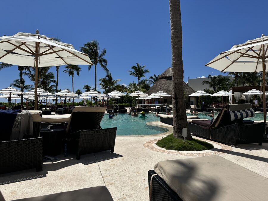 Umbrellas and lounge chairs surround a pool on a clear, sunny day. 