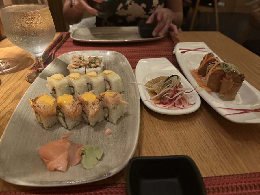 Three sushi rolls of various fishes with sides of white tuna and spring rolls. 