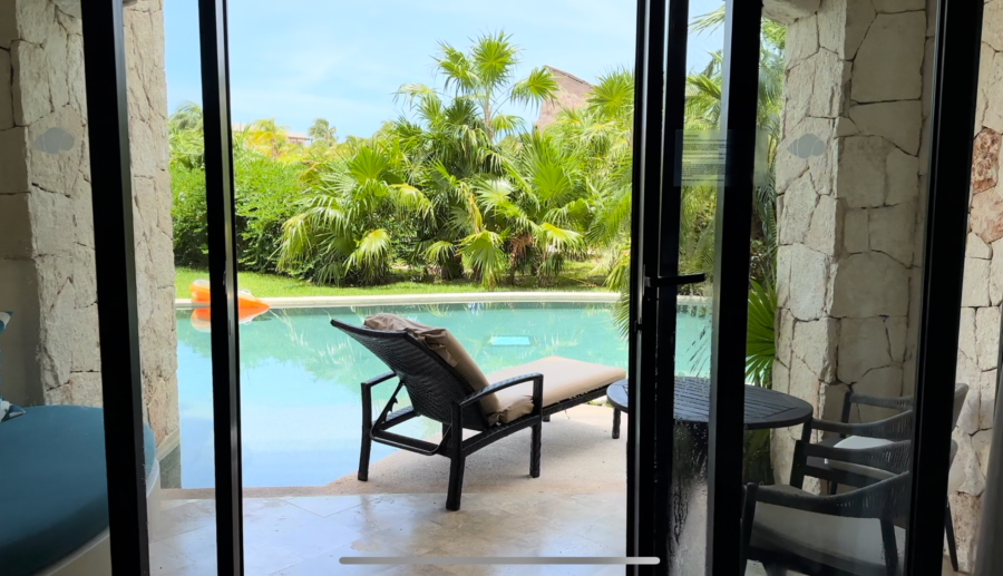 A window looks out over a pool, which is behind a brown lounge chair. 